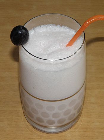 фото вкусного молочного коктейля с коньяком в бокале с трубочкой и виноградинкой
