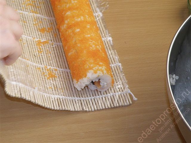 Поднимите нижний край циновки вместе с листом нори, закройте начинку и аккуратно прокатите коврик