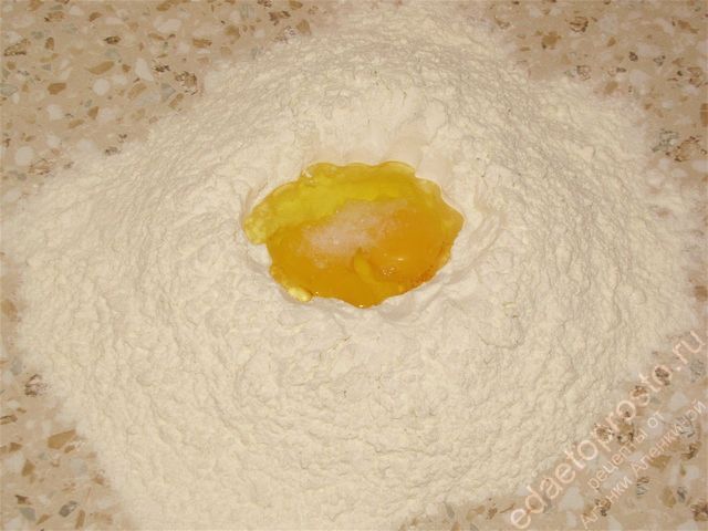 Высыпать на стол половину муки и добавить яйца с солью