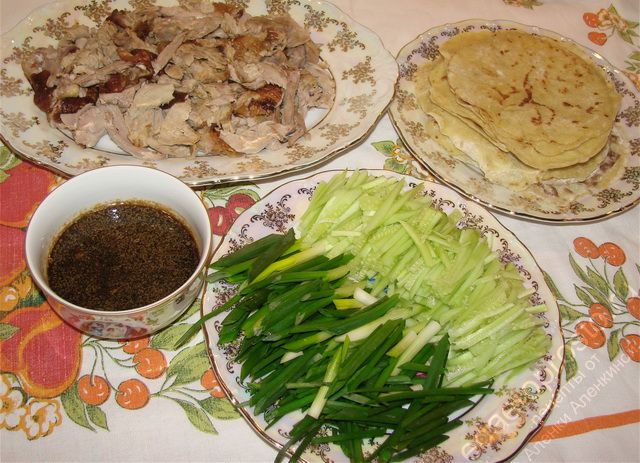 фото сервировки утки по-пекински с блинчиками для мандаринов, овощами и соусом на столе
